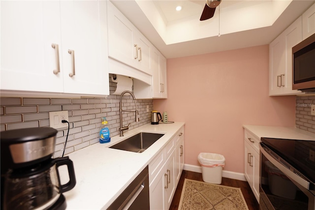 kitchen with sink, white cabinets, ceiling fan, a tray ceiling, and stainless steel appliances