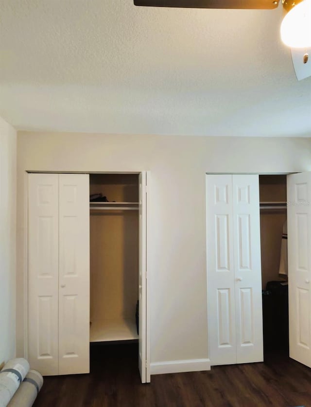 unfurnished bedroom with dark hardwood / wood-style flooring, a textured ceiling, and multiple closets