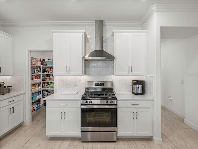 kitchen featuring crown molding, white cabinets, wall chimney range hood, and stainless steel range with gas stovetop