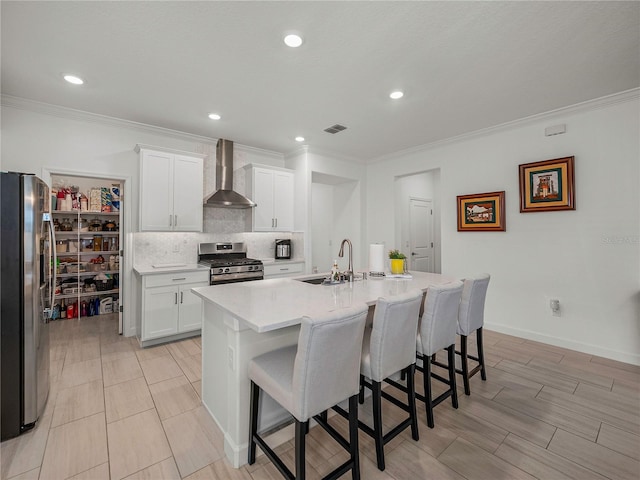 kitchen featuring wall chimney exhaust hood, stainless steel appliances, sink, white cabinetry, and an island with sink