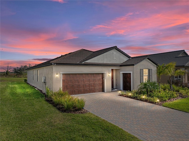 ranch-style house with a garage, a lawn, decorative driveway, and stucco siding