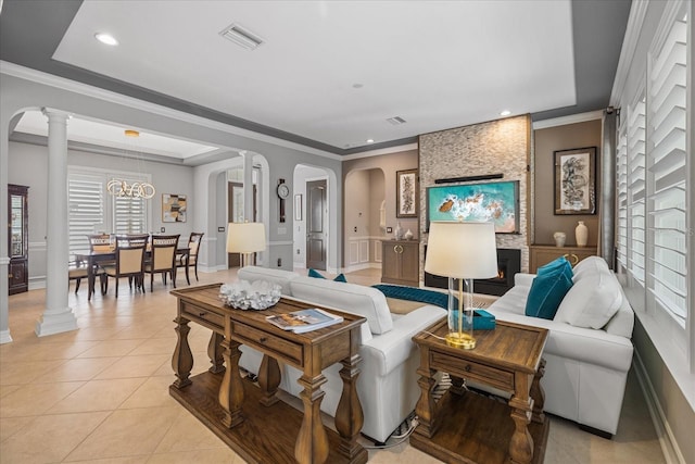 tiled living room featuring a stone fireplace, a raised ceiling, crown molding, and a chandelier