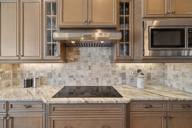 kitchen with black electric cooktop, decorative backsplash, stainless steel microwave, and wall chimney range hood