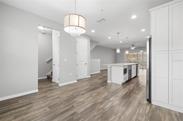 kitchen featuring ceiling fan, hanging light fixtures, dark hardwood / wood-style flooring, a center island with sink, and white cabinets