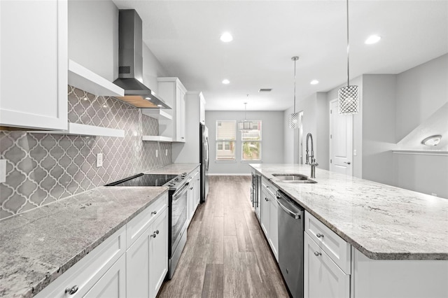 kitchen featuring appliances with stainless steel finishes, sink, wall chimney range hood, decorative light fixtures, and white cabinets