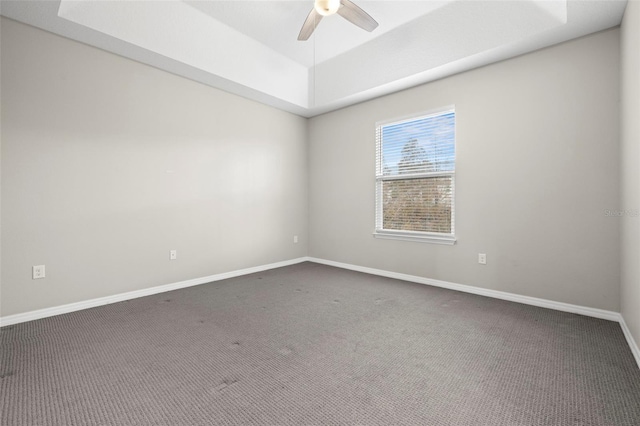 spare room with a tray ceiling, ceiling fan, and dark carpet