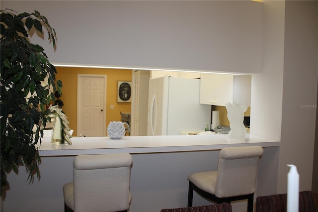 kitchen featuring kitchen peninsula, white refrigerator, a kitchen bar, and white cabinetry