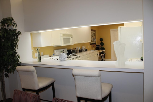 kitchen with kitchen peninsula, a kitchen breakfast bar, white appliances, and white cabinetry