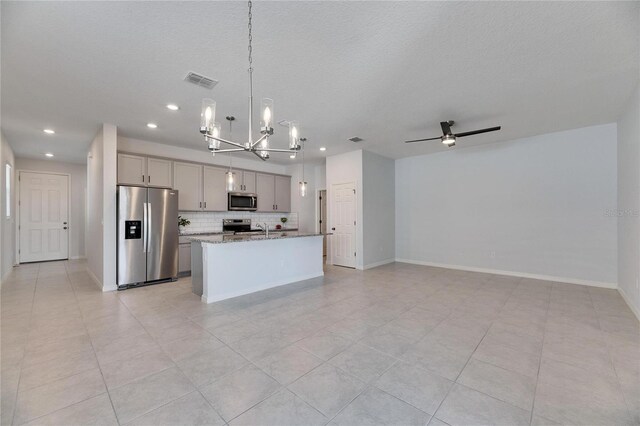 kitchen featuring light stone countertops, appliances with stainless steel finishes, pendant lighting, gray cabinets, and an island with sink