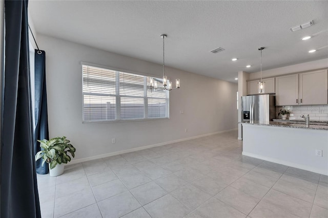 kitchen with light stone countertops, decorative backsplash, a chandelier, stainless steel fridge with ice dispenser, and gray cabinets