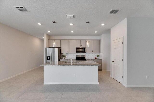 kitchen featuring appliances with stainless steel finishes, a center island with sink, gray cabinets, and hanging light fixtures