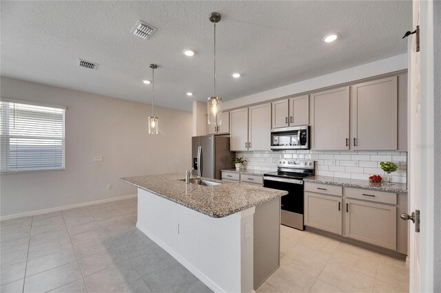 kitchen with decorative light fixtures, light stone counters, an island with sink, and appliances with stainless steel finishes