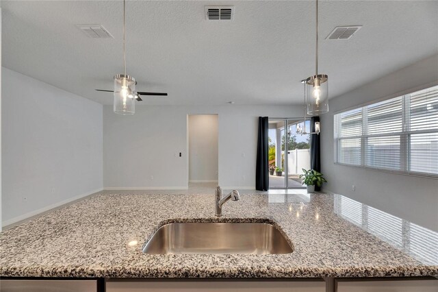 kitchen with pendant lighting, light stone countertops, sink, and a textured ceiling