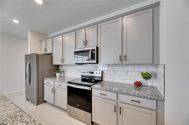 kitchen with light stone countertops, stainless steel appliances, tasteful backsplash, a textured ceiling, and gray cabinets