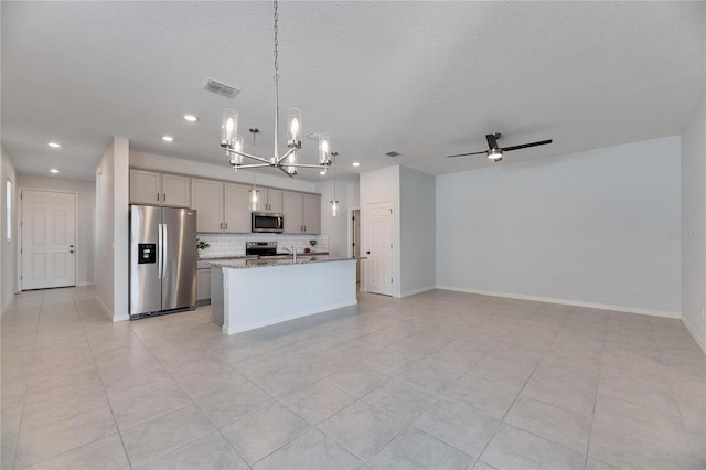 kitchen featuring hanging light fixtures, appliances with stainless steel finishes, an island with sink, gray cabinetry, and light stone counters