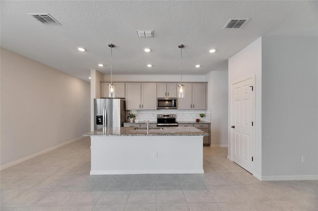 kitchen with appliances with stainless steel finishes, gray cabinetry, hanging light fixtures, and an island with sink