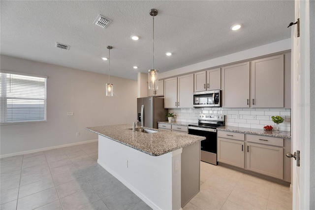 kitchen with a center island with sink, stainless steel appliances, light stone counters, and decorative light fixtures