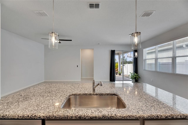 kitchen with light stone counters, sink, hanging light fixtures, and a textured ceiling