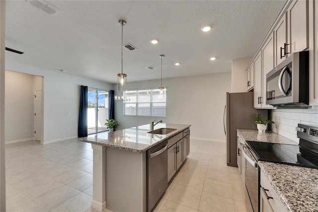 kitchen featuring an island with sink, stainless steel appliances, hanging light fixtures, light stone countertops, and sink