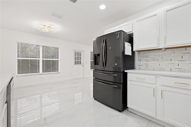 kitchen featuring black fridge, white cabinetry, light stone counters, and tasteful backsplash