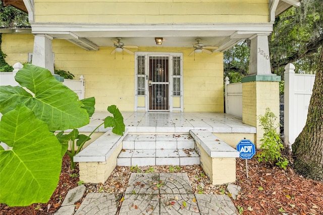 view of exterior entry with ceiling fan and fence