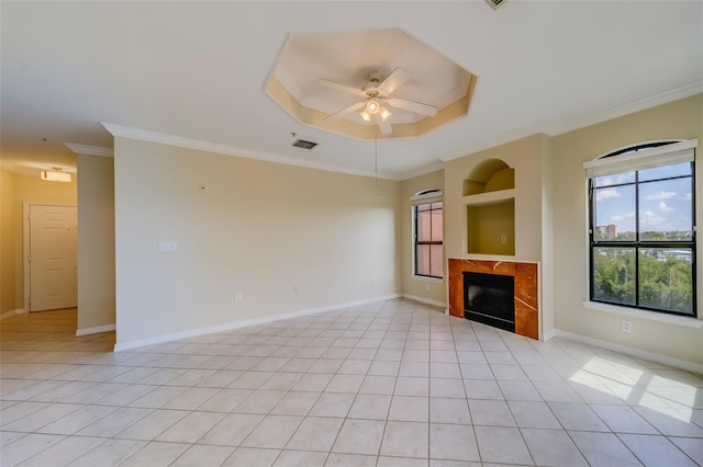 unfurnished living room featuring a raised ceiling, ceiling fan, light tile patterned floors, ornamental molding, and built in shelves