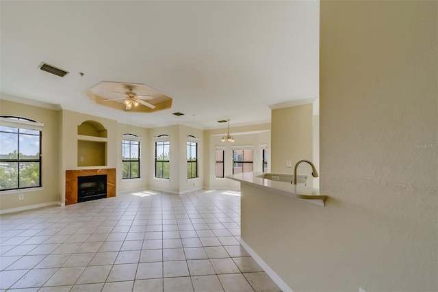 unfurnished living room with ceiling fan with notable chandelier, a tile fireplace, ornamental molding, and light tile patterned floors