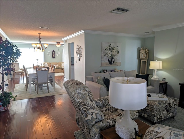 living area featuring a textured ceiling, ornamental molding, dark wood-style flooring, and visible vents