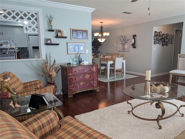 living room with a notable chandelier, dark wood-type flooring, a textured ceiling, and ornamental molding