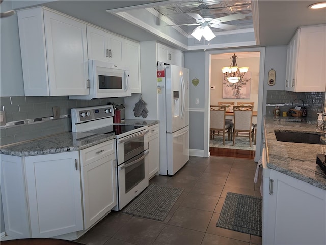 kitchen with backsplash, white appliances, a tray ceiling, sink, and white cabinets