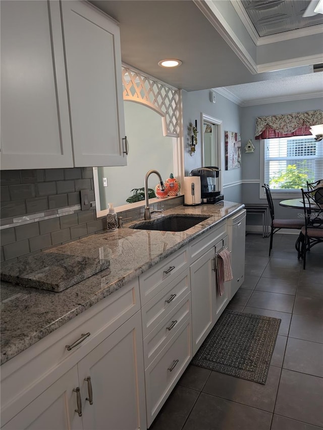 kitchen with light stone countertops, sink, dark tile patterned floors, white cabinets, and ornamental molding