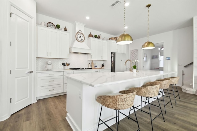 kitchen featuring white cabinets, decorative light fixtures, a kitchen island with sink, and backsplash