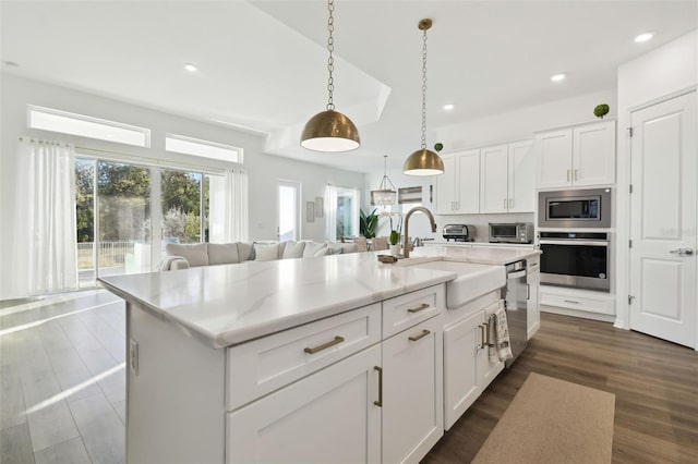 kitchen featuring white cabinetry, decorative light fixtures, stainless steel appliances, and a center island with sink