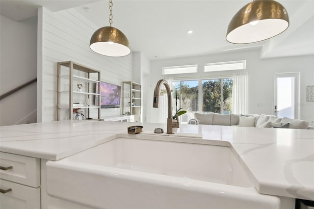 kitchen with light stone countertops, sink, pendant lighting, and white cabinets