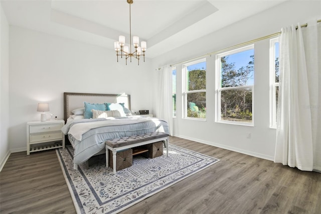 bedroom with dark wood-type flooring, a tray ceiling, and a chandelier