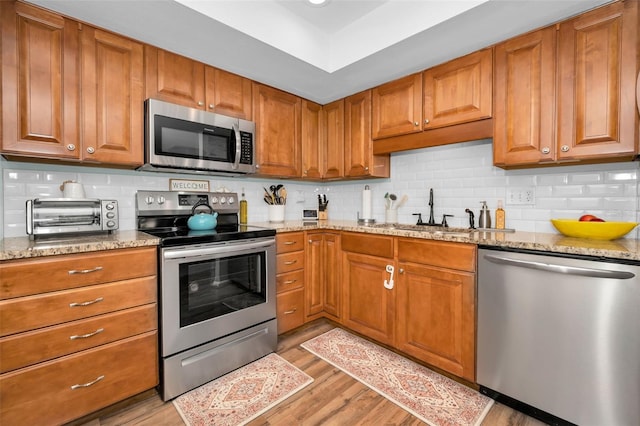 kitchen featuring sink, decorative backsplash, light stone countertops, light hardwood / wood-style floors, and stainless steel appliances