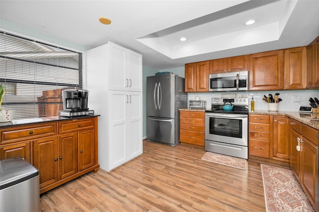 kitchen featuring light stone countertops, stainless steel appliances, light hardwood / wood-style flooring, and a tray ceiling