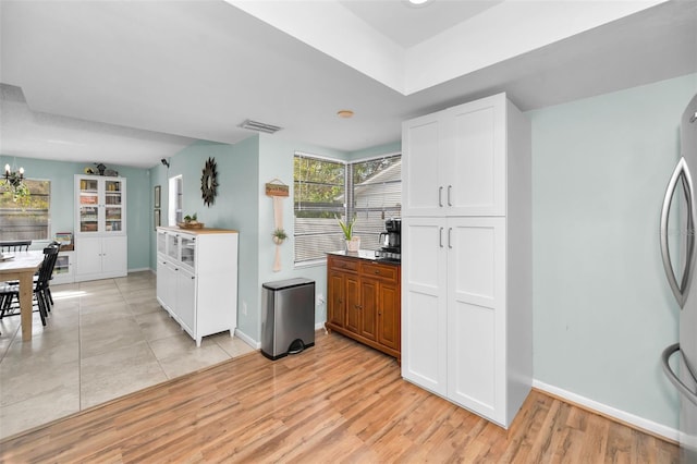 kitchen with stainless steel refrigerator, white cabinetry, light hardwood / wood-style floors, and an inviting chandelier