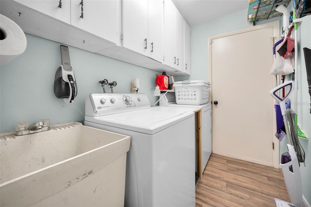 laundry room with cabinets, washing machine and dryer, light wood-type flooring, and sink