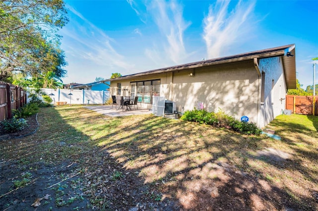 rear view of property featuring a lawn, cooling unit, and a patio