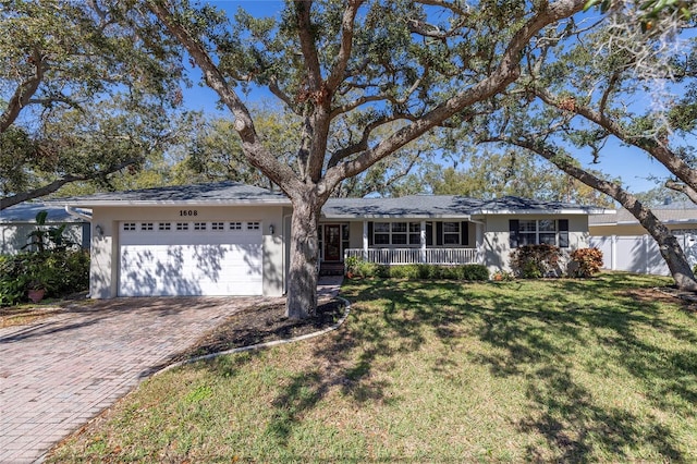 ranch-style house featuring decorative driveway, covered porch, fence, a garage, and a front lawn