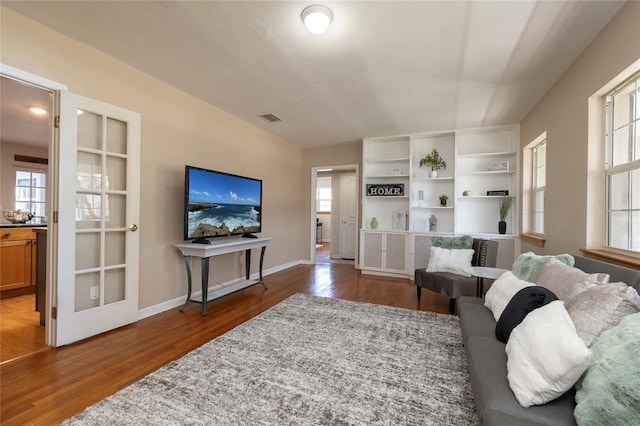 living area featuring visible vents, plenty of natural light, baseboards, and wood finished floors