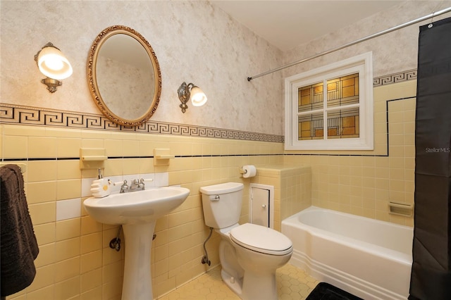 full bathroom featuring toilet, tile walls, wainscoting, tile patterned floors, and wallpapered walls