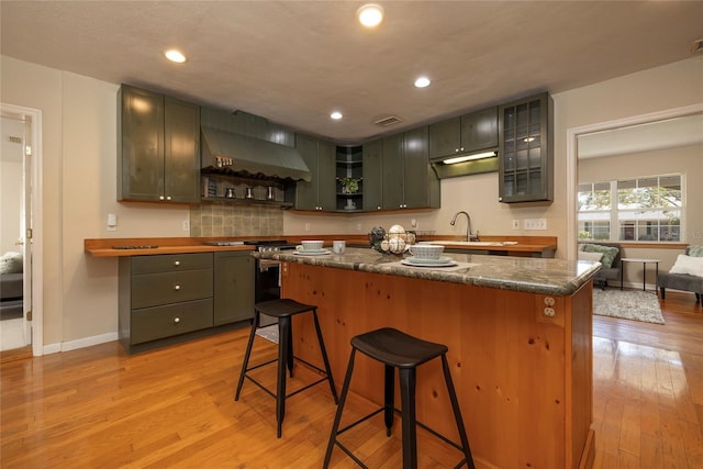 kitchen with wall chimney exhaust hood, light wood-style flooring, a kitchen breakfast bar, stainless steel gas range, and a sink