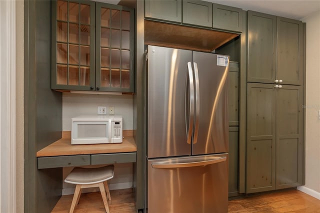 kitchen featuring white microwave, light wood-style flooring, light countertops, freestanding refrigerator, and glass insert cabinets