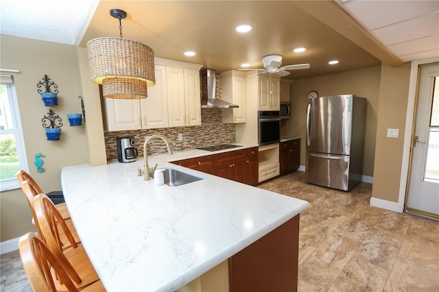 kitchen with kitchen peninsula, appliances with stainless steel finishes, sink, wall chimney range hood, and hanging light fixtures