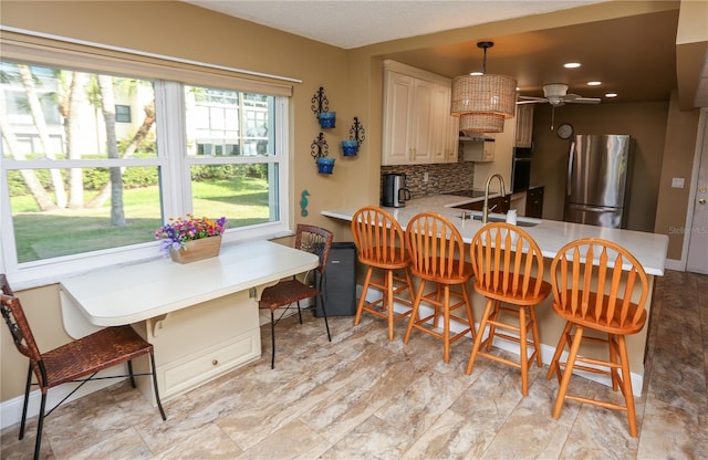 kitchen featuring a breakfast bar, sink, tasteful backsplash, kitchen peninsula, and stainless steel refrigerator