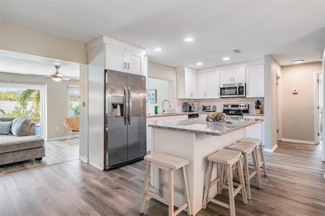 kitchen featuring white cabinets, light stone countertops, a breakfast bar area, and appliances with stainless steel finishes