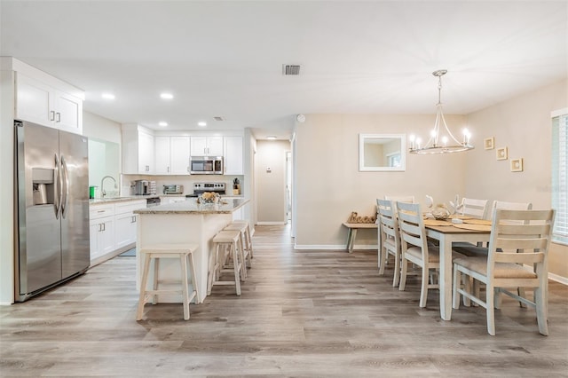 kitchen with light stone countertops, appliances with stainless steel finishes, white cabinets, a center island, and hanging light fixtures