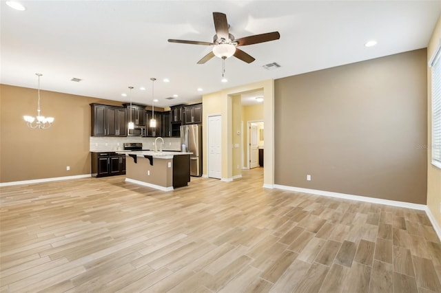 kitchen with a breakfast bar, stainless steel appliances, hanging light fixtures, and a center island with sink